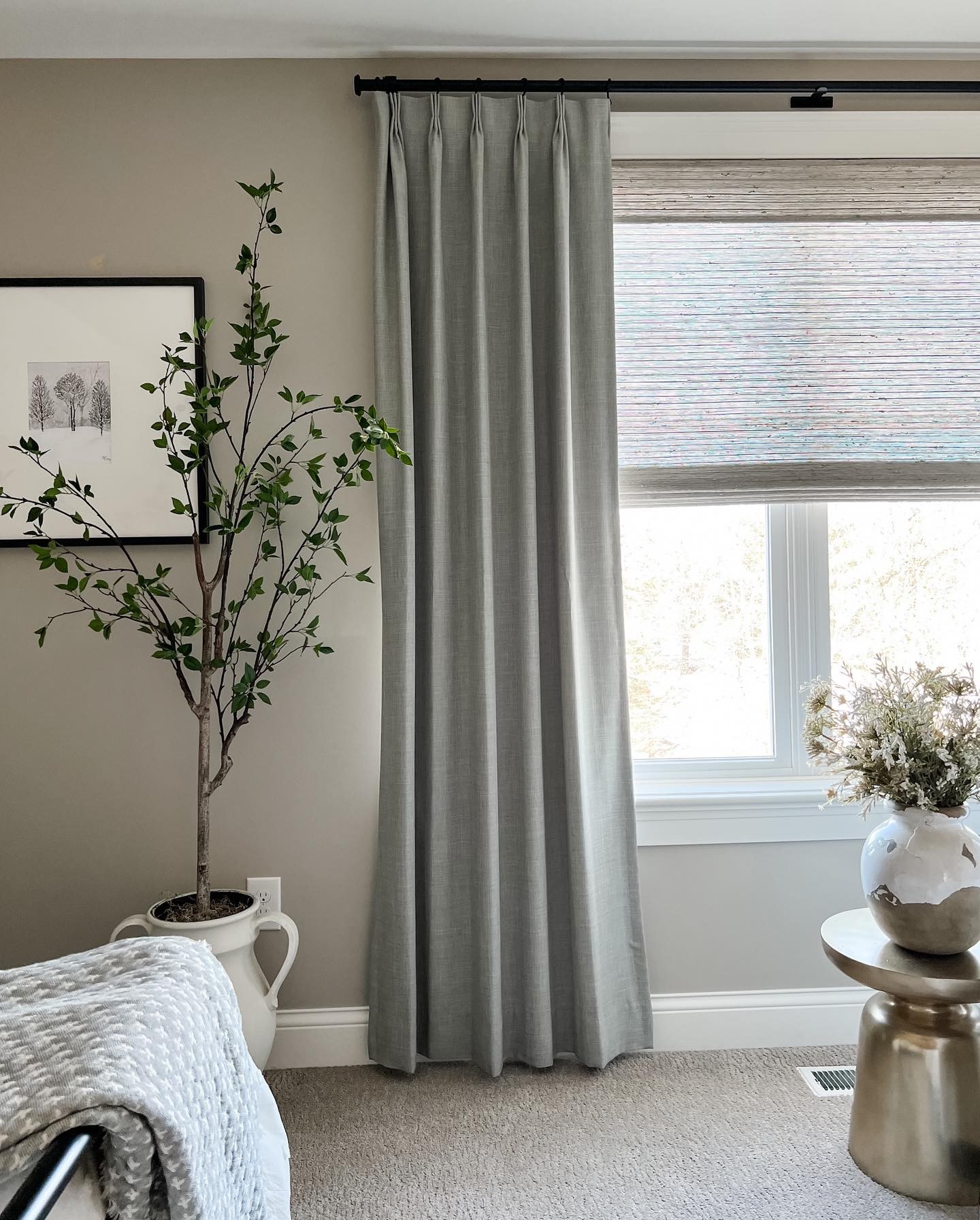 a bedroom with easy classic pleat drapery in rio stone and woven wood shades in bennett mist
