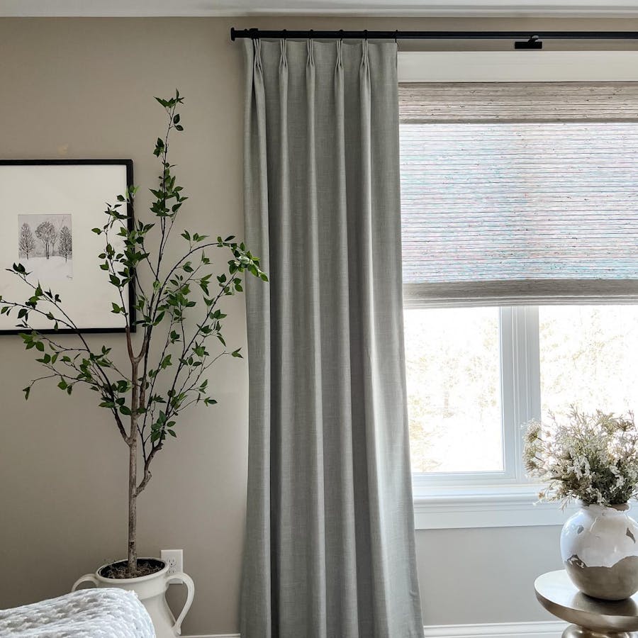a bedroom with easy classic pleat drapery in rio stone and woven wood shades in bennett mist