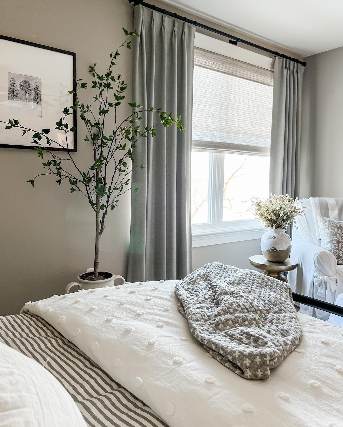 a bedroom with easy classic pleat drapery in rio stone and woven wood shades in bennett mist