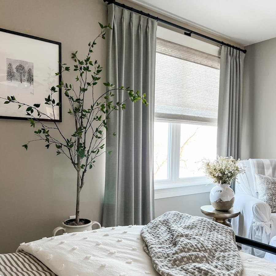 a bedroom with easy classic pleat drapery in rio stone and woven wood shades in bennett mist
