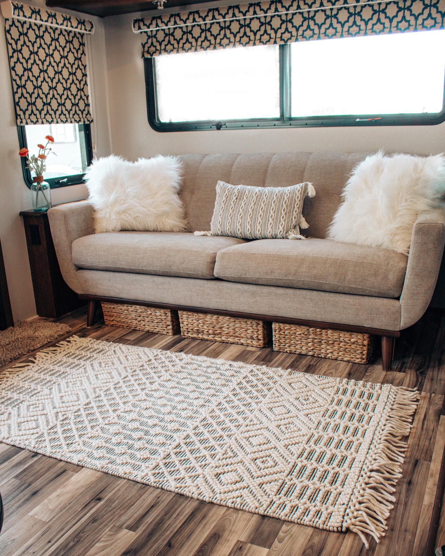 Gray sofa with white pillows inside an RV. There are Premium Decorative Roller Shades on the windows.