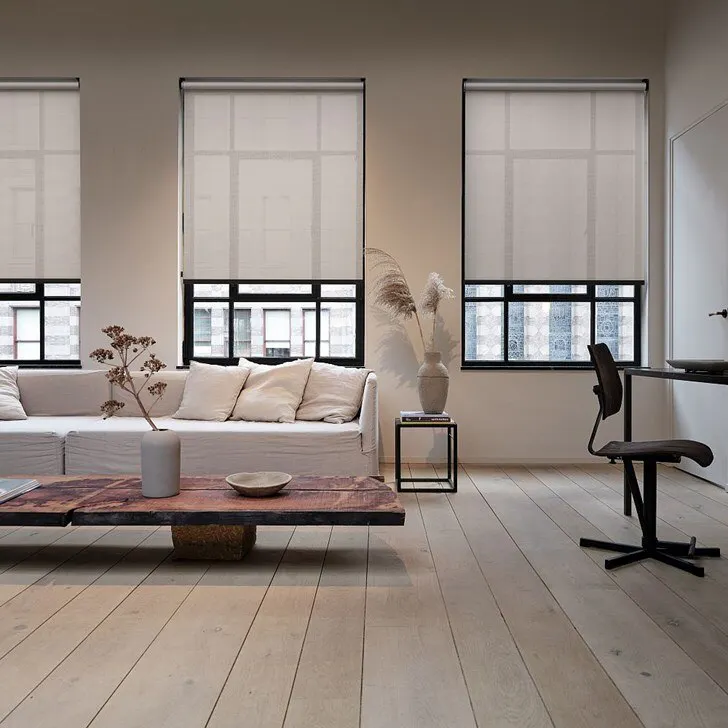 Eve MotionBlinds Motorized Light Filtering Roller Shades on three tall windows in a modern, neutral living room with a cream sofa and minimalist furnishings.