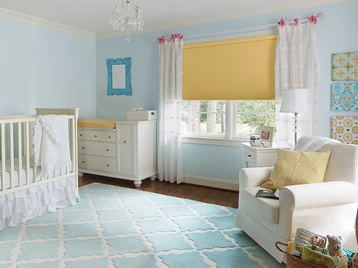Nursery with pastel blue walls and yellow cellular shades.