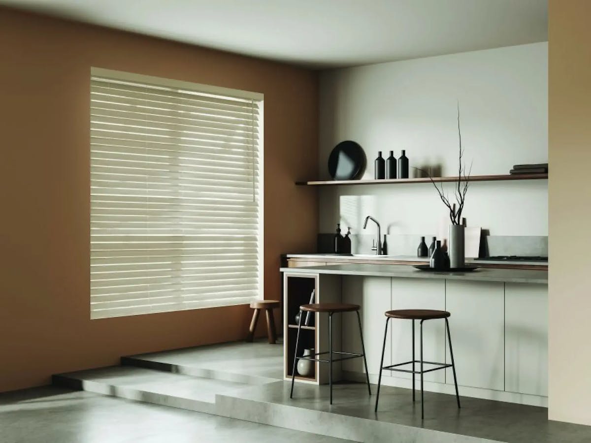 Kitchenette with a brown accent wall. The accent wall has a large window covered with white faux wood blinds. The kitchenette has neutral tones and light brown wood accents.