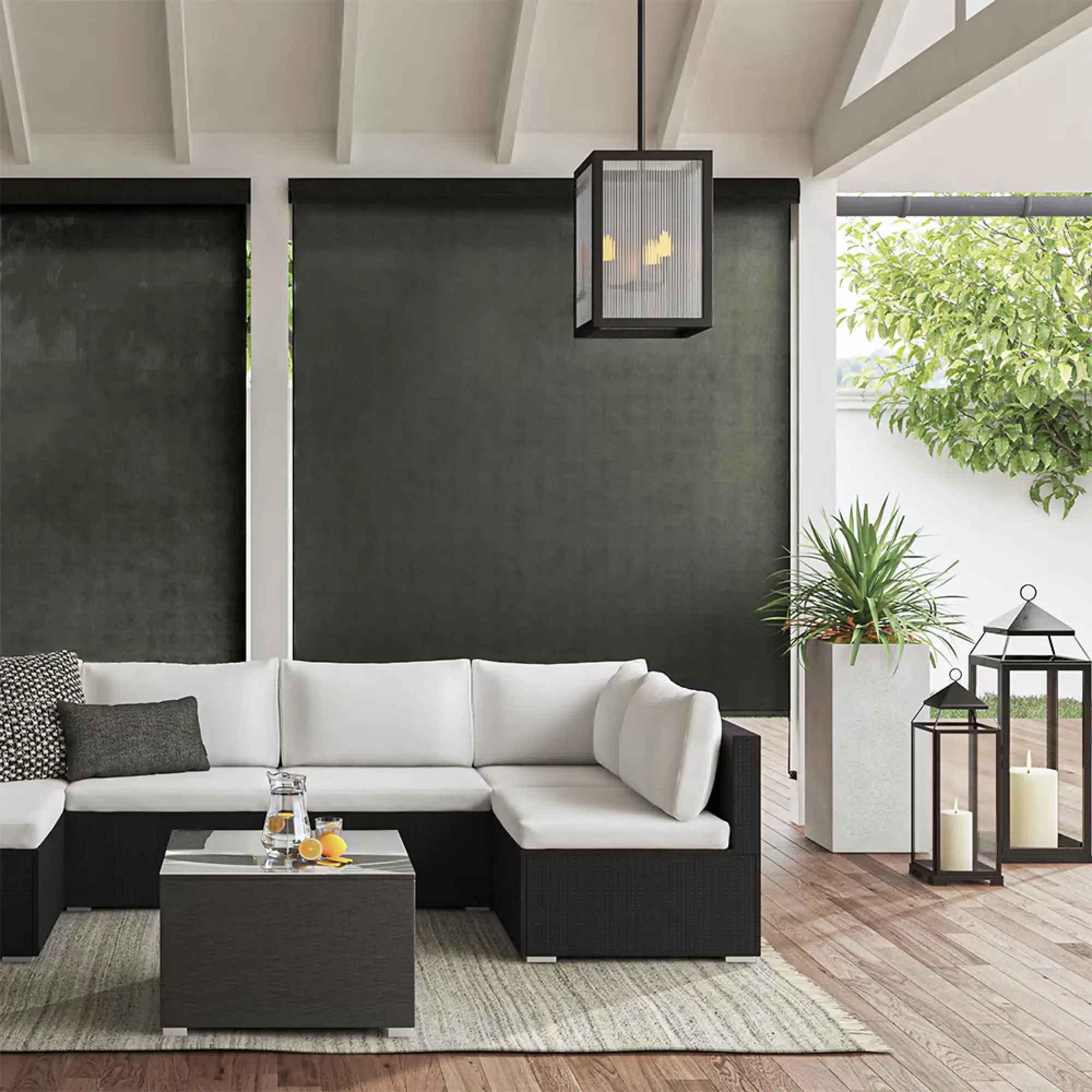 Outdoor patio with black and white furniture. There's a U-shaped couch with a glass-top coffee table in the center. Underneath the furniture is a gray woven rug. Behind the couch are white pillars with black outdoor shades.