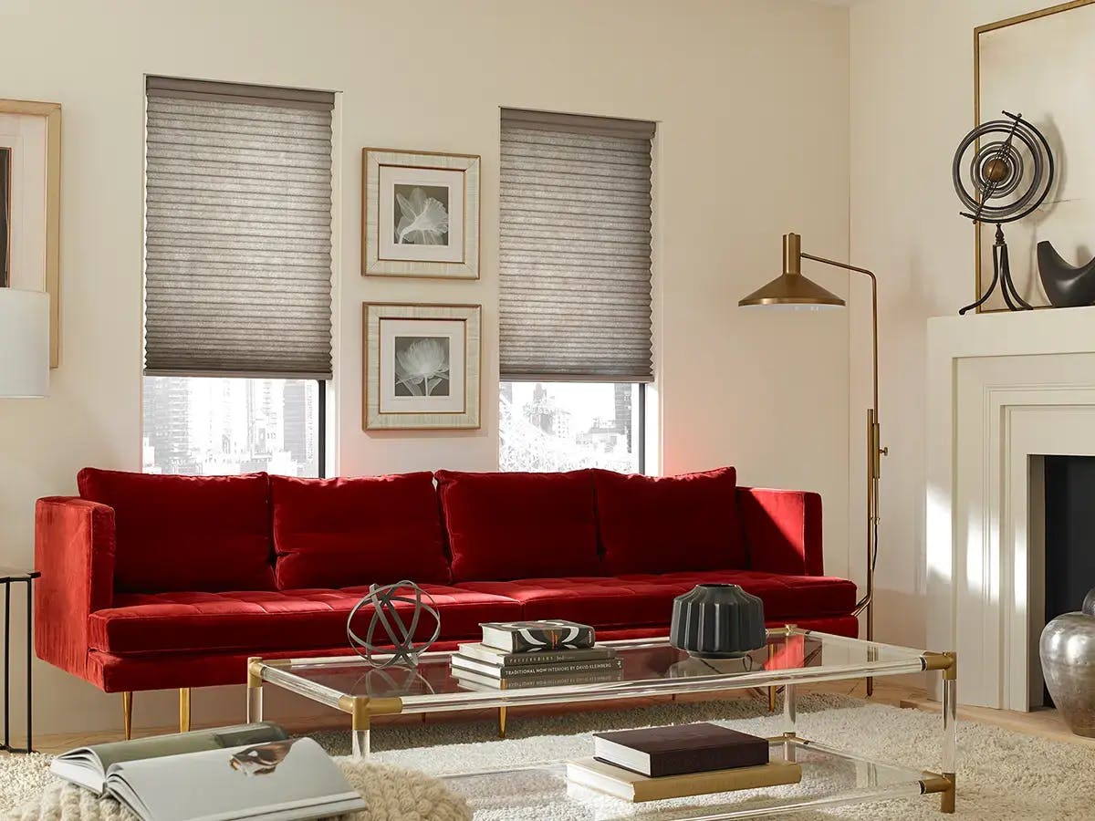 Living room featuring a red couch in front of windows that have neutral-colored cellular shades.