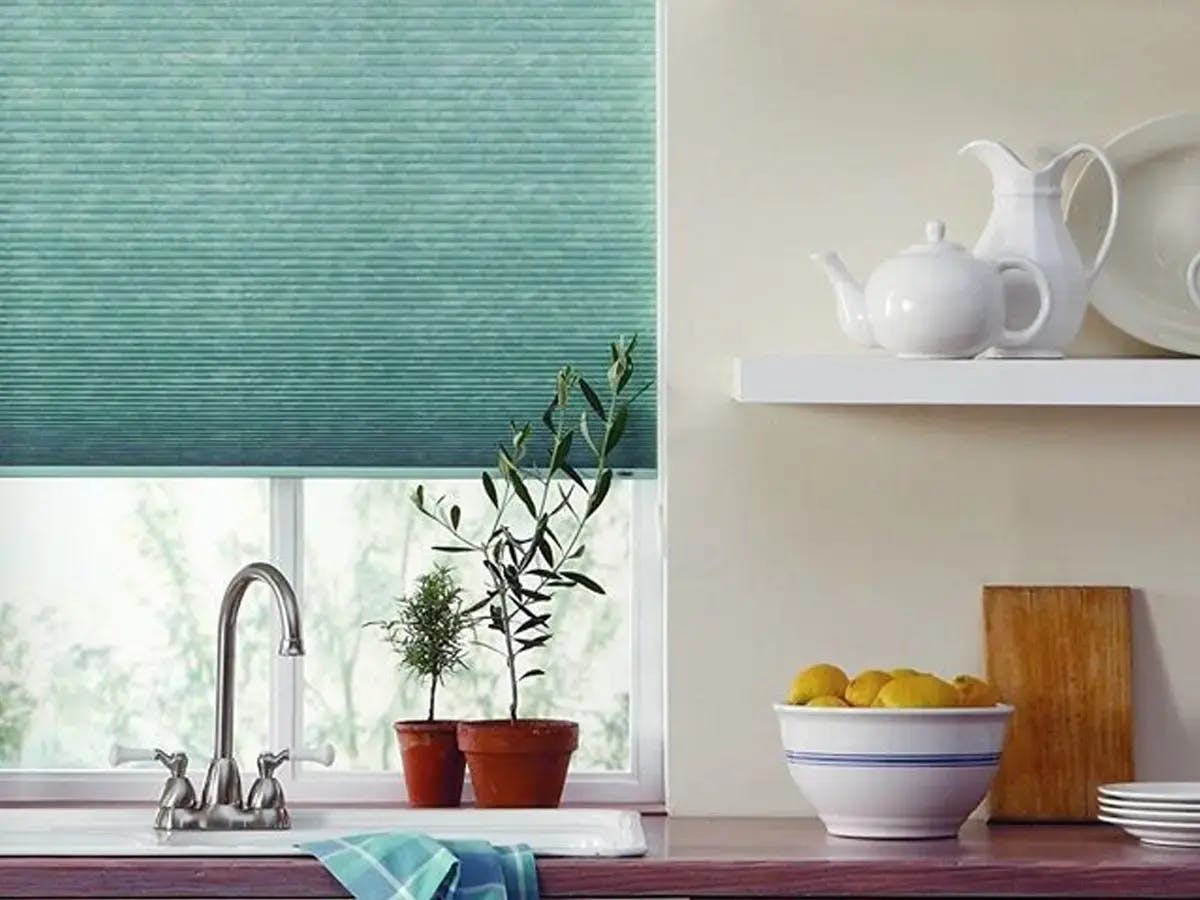 A kitchen sink with plants, lemons in a bowl, and a teal window shade.