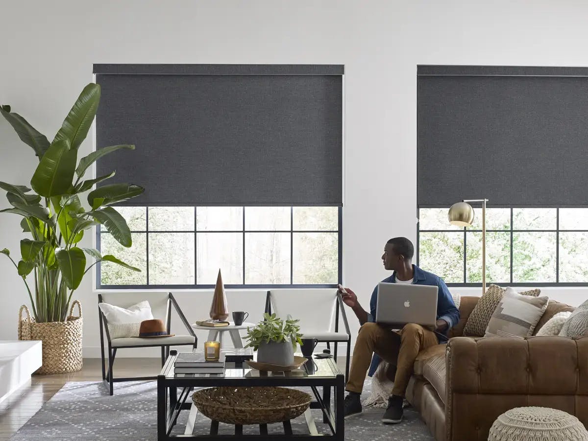 Man using remote to adjust black roller shades in a living room.