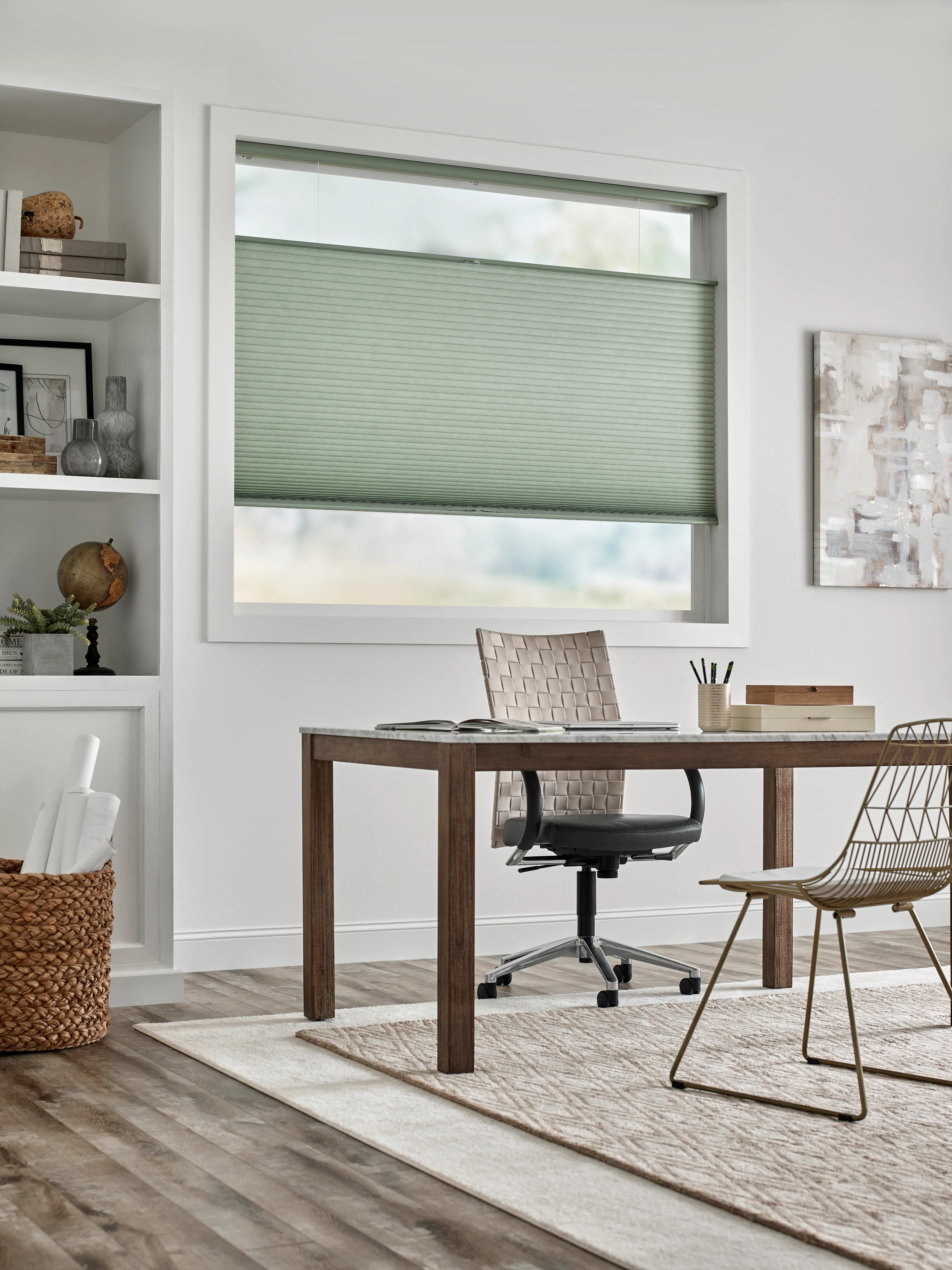 Office with white walls, a desk and cellular shades in a muted seafoam green color.