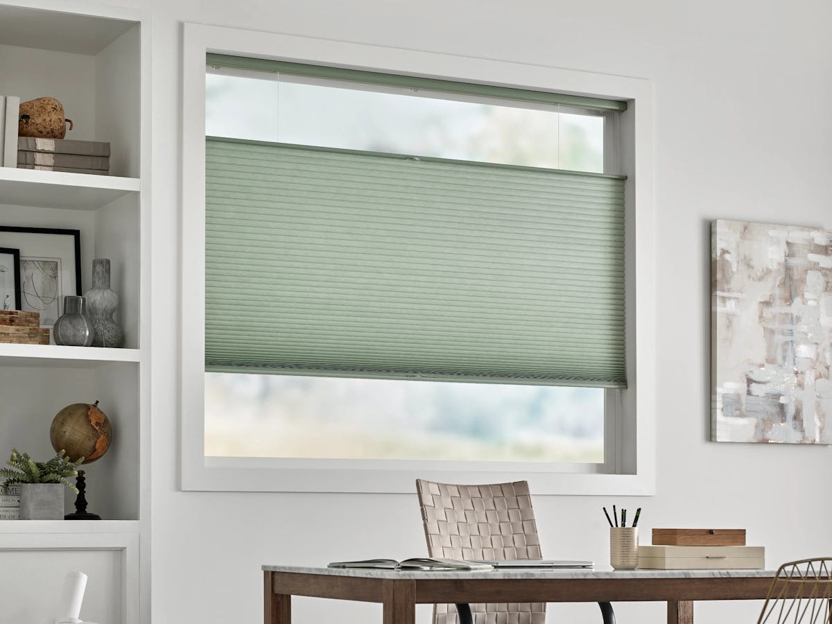 Office with white walls, a desk and cellular shades in a muted seafoam green color.