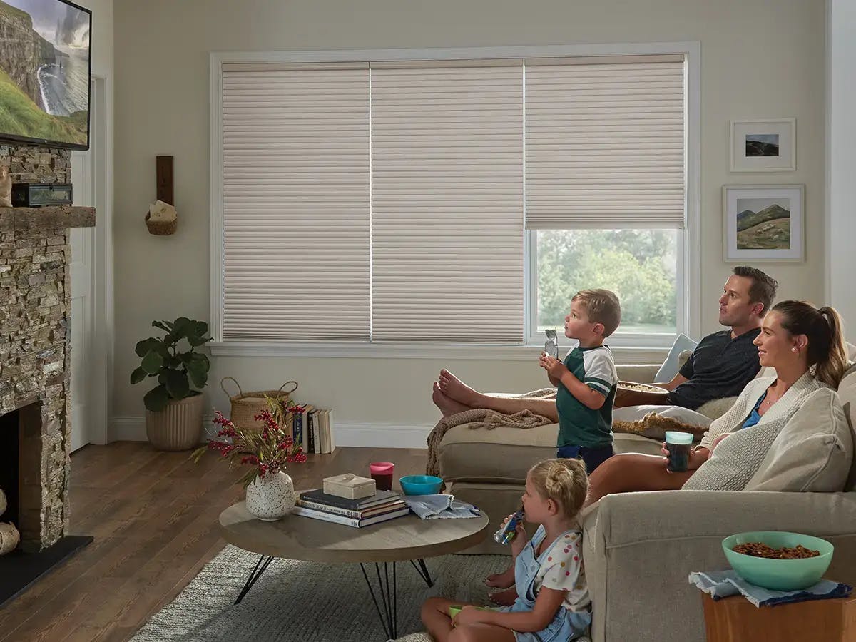 Family of four seated in living room looking at the tv screen with cellular shades on the windows.