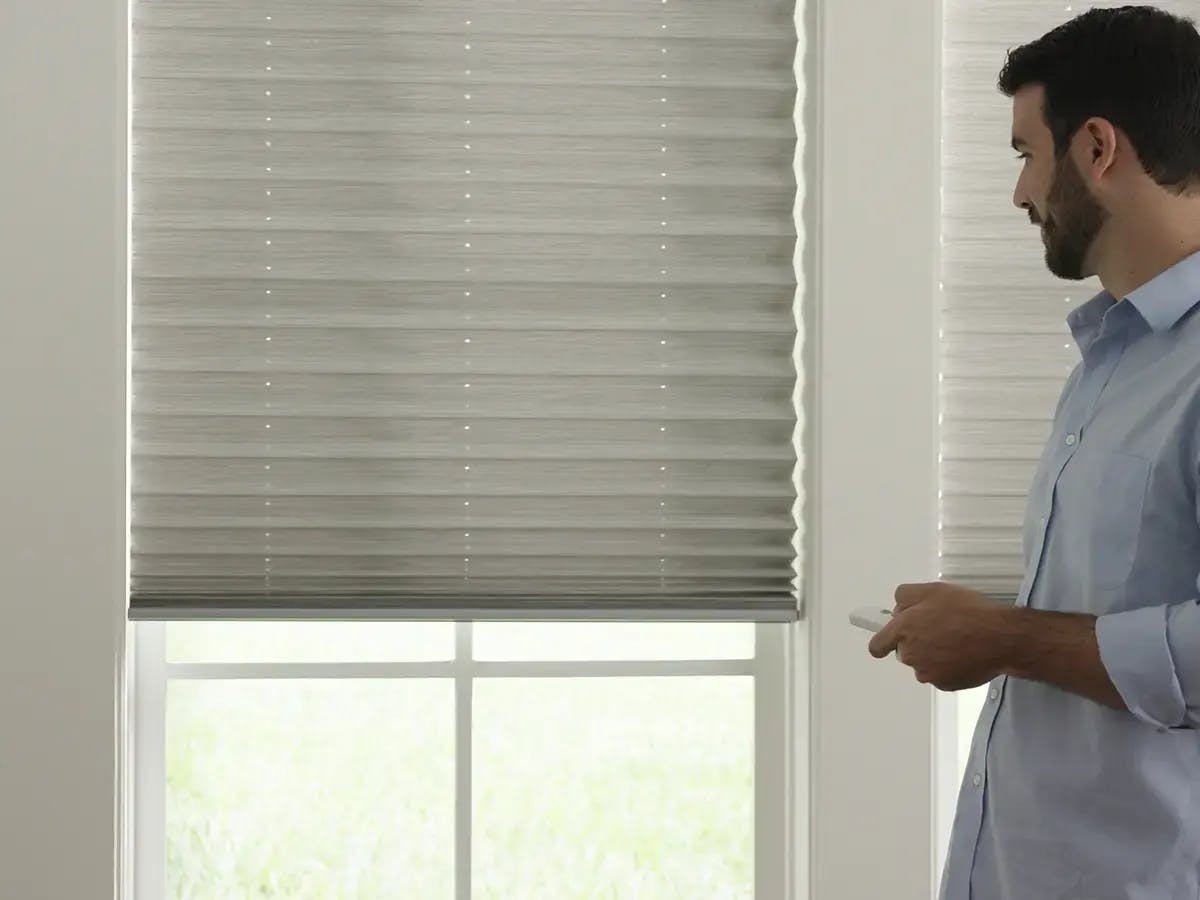 A man holding a remote towards motorized blinds.