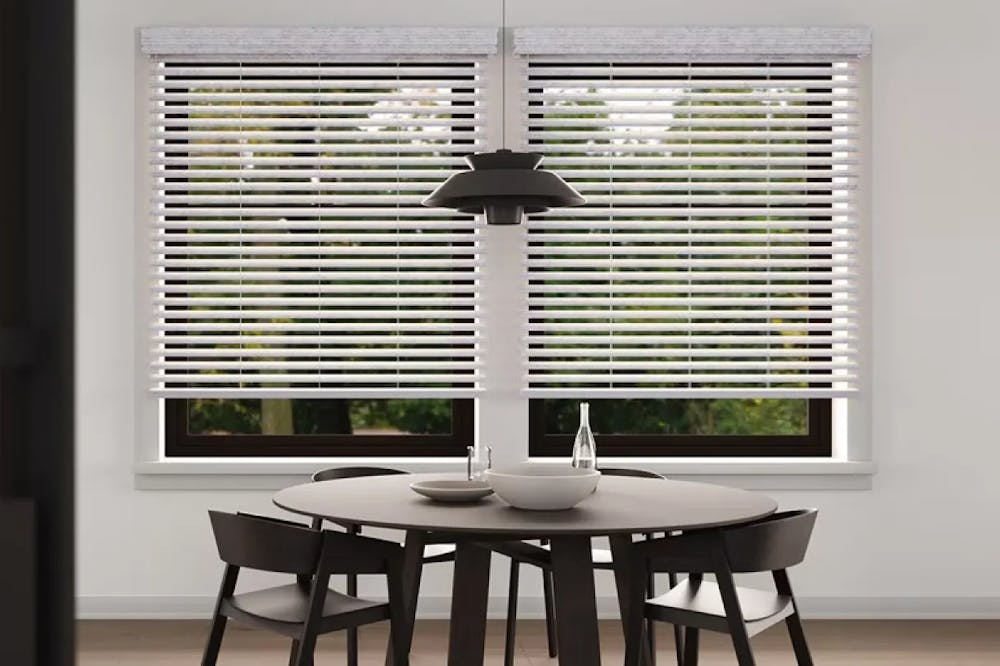 Dining room with a dark wood table and four chairs, black pendant light and a wide window with white faux wood blinds.