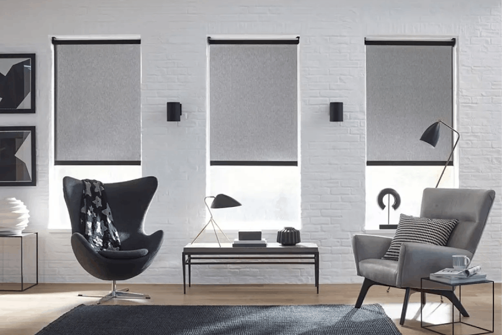 A modern sitting area with a gray and black color scheme. The windows have gray solar roller shades pulled halfway down.