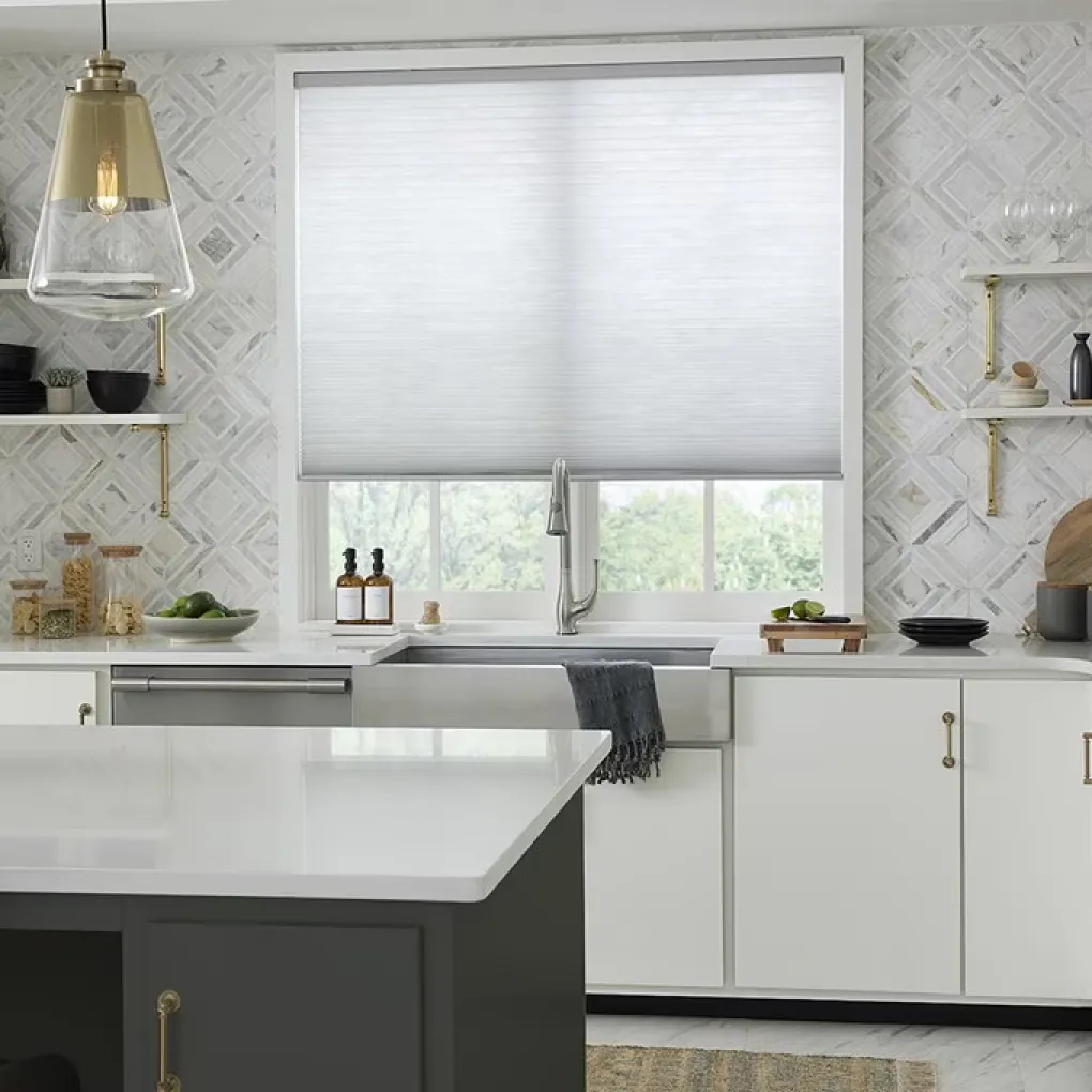 Kitchen with white counters, aluminum and brass hardware, and a window over the sink with white, light-filtering cellular shades.