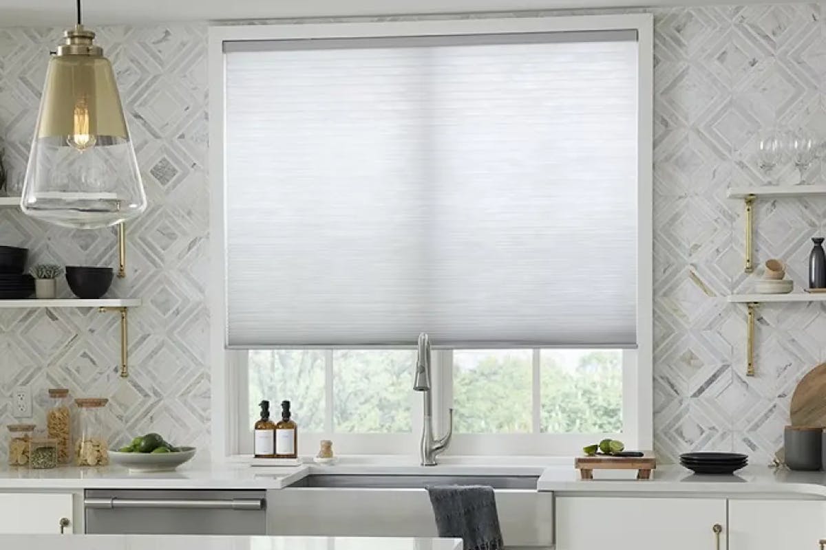 Kitchen with white counters, aluminum and brass hardware, and a window over the sink with white, light-filtering cellular shades.