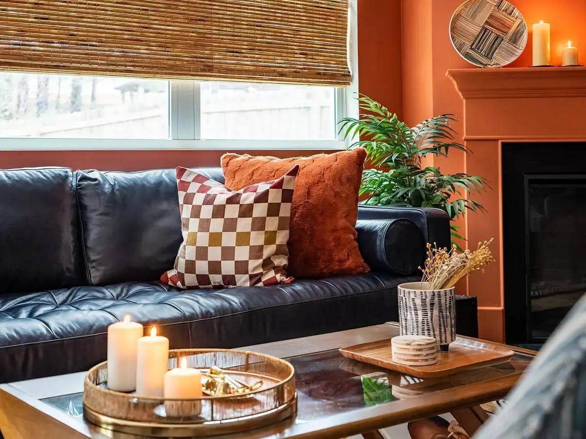 Living room area with black couch, orange and brown pillows and woven wood shades.