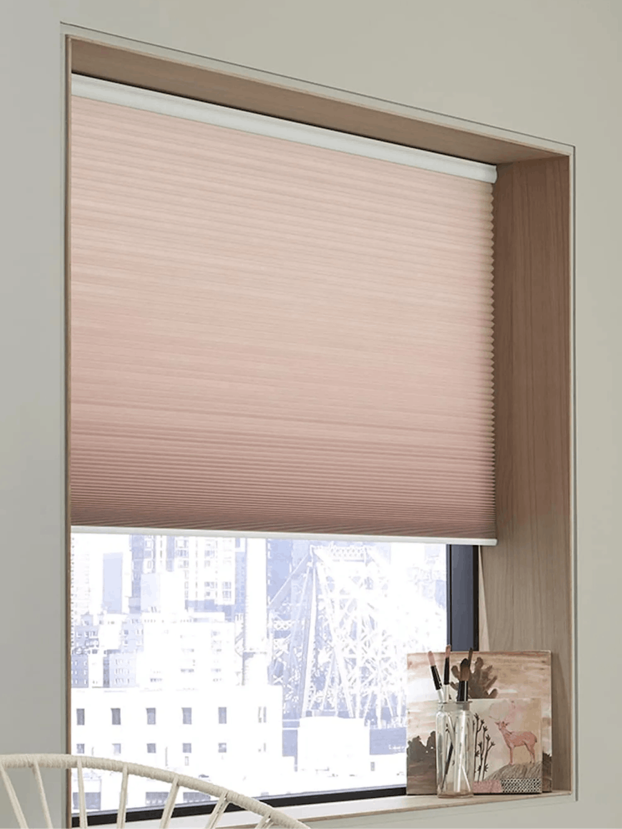 Window with pink, light-filtering cellular shades. There’s small decor on the windowsill.