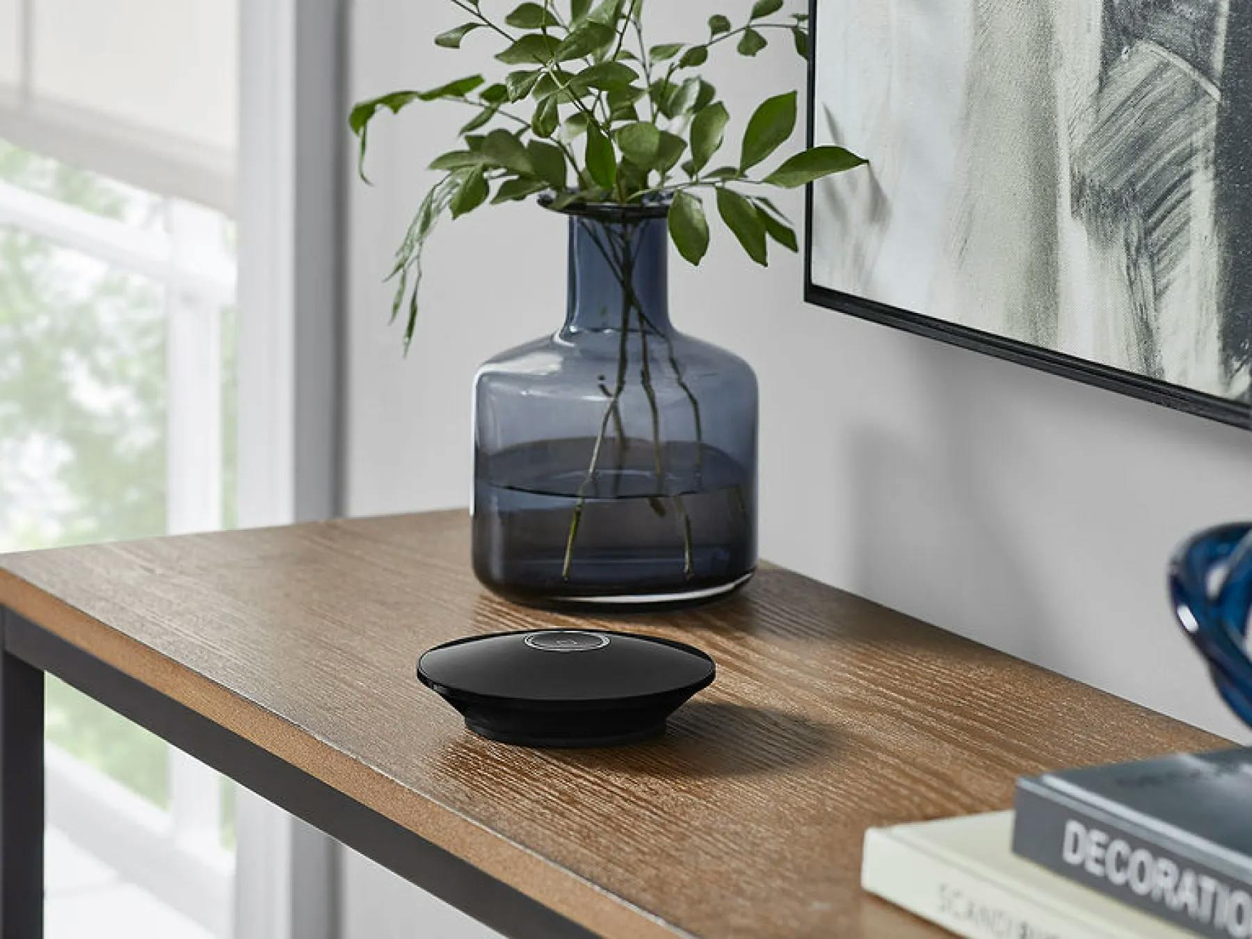 A smart home hub sits on a brown table. The table also has various decorations on it.