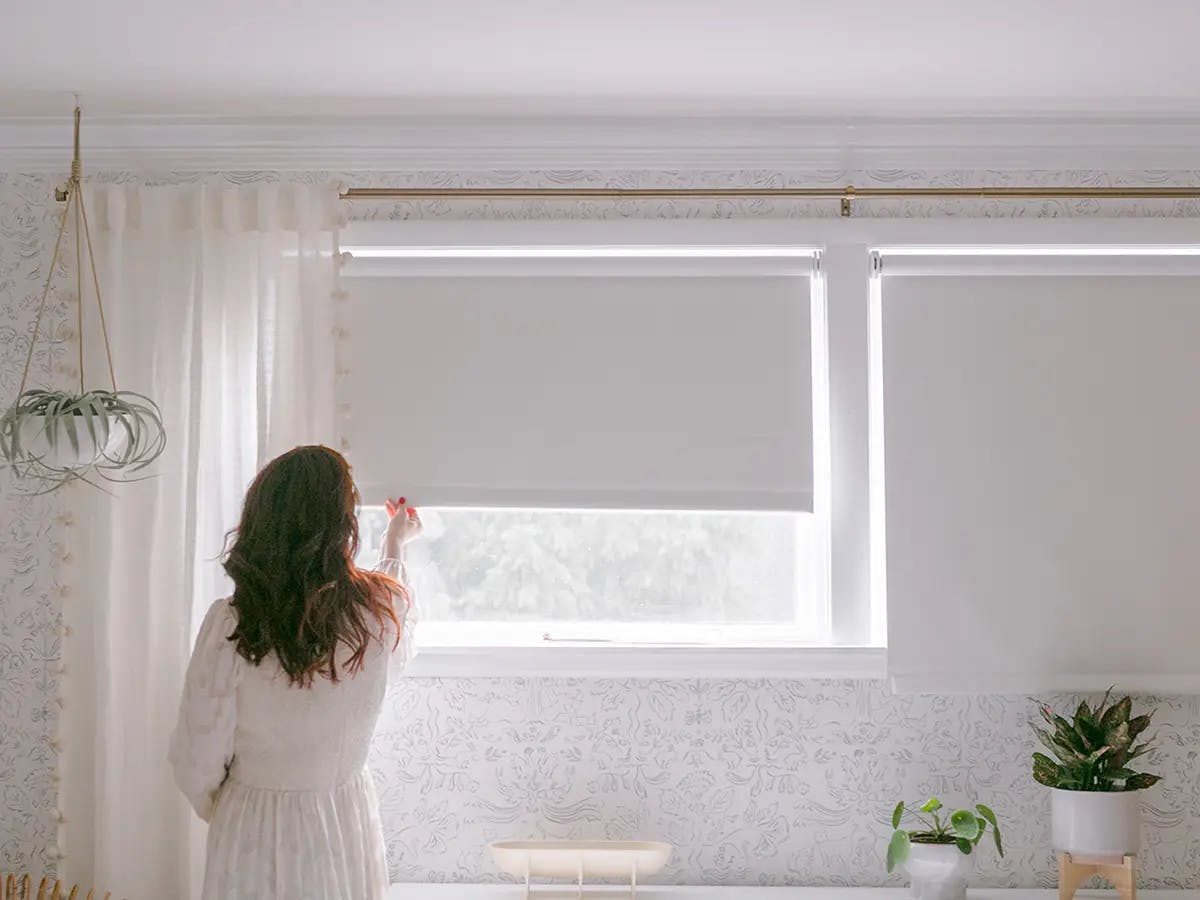 Woman pulling down blackout roller shades.