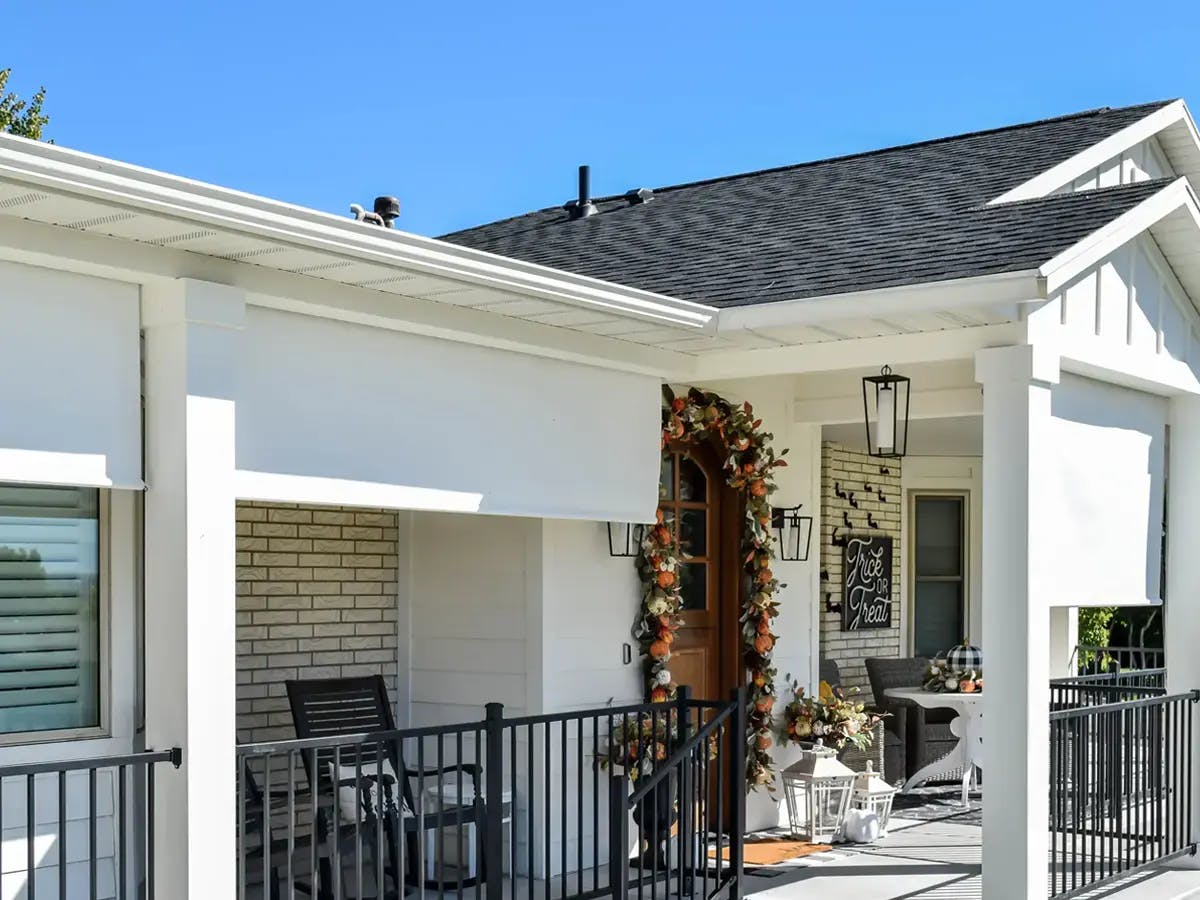 A white porch decorated for fall with pumpkins, leaves, and a 