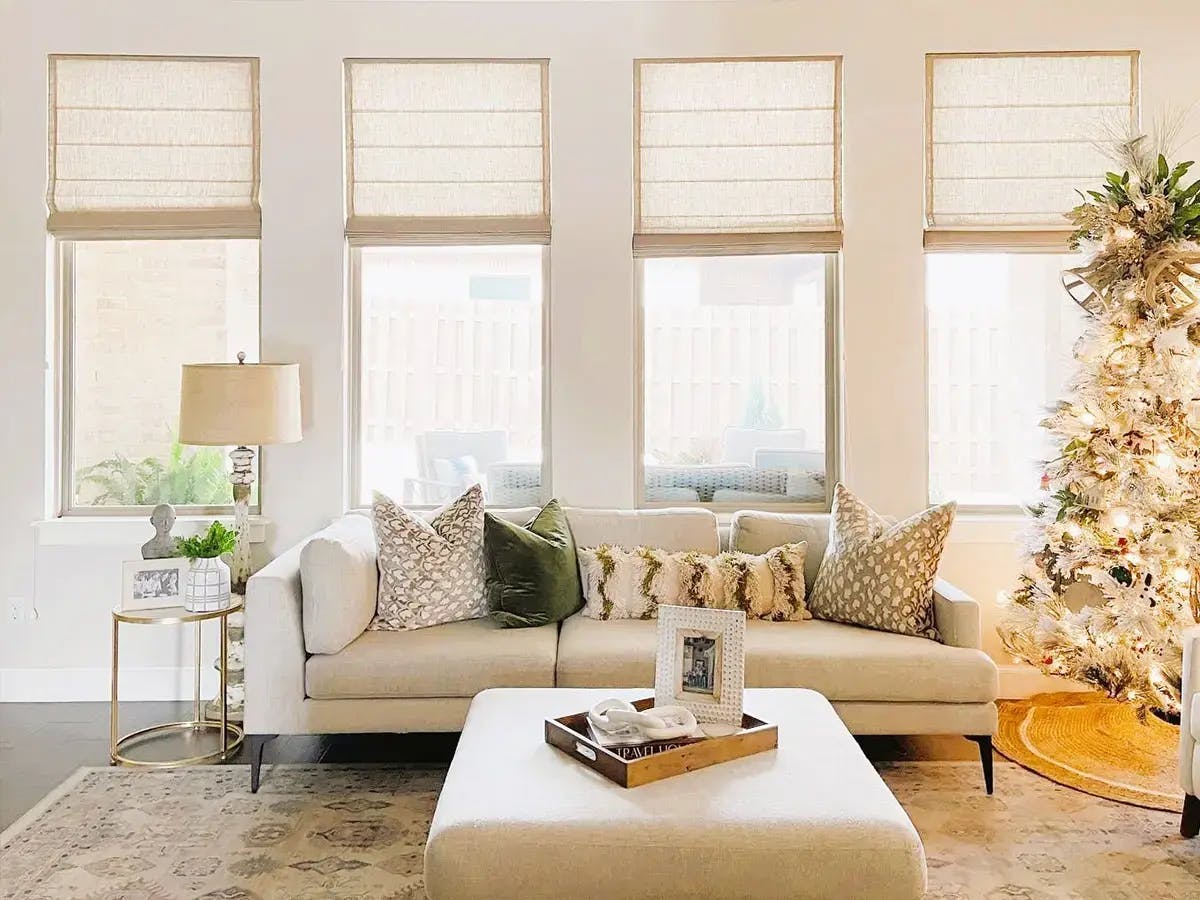 A bright living room featuring a white sofa, patterned pillows, and a Christmas tree.