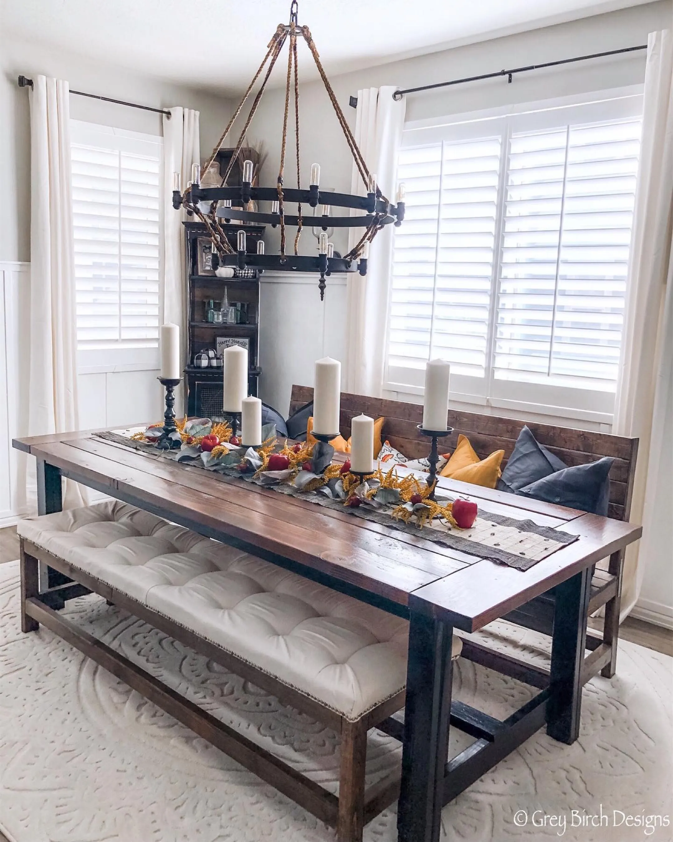 Dining room with white interior shutters, a wooden dining table with wooden benches and fall decor on the table.