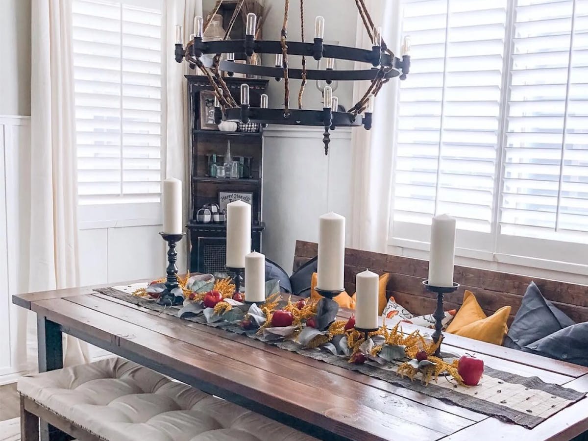 Dining room with white interior shutters, a wooden dining table with wooden benches and fall decor on the table.