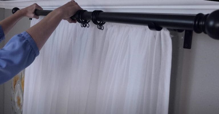 Woman hanging black metal curtain rod