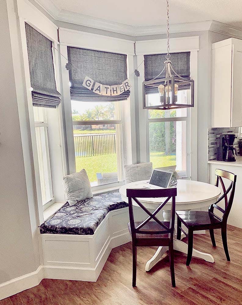 dining room bay window with cushioned window seat and grey linen roman shades.