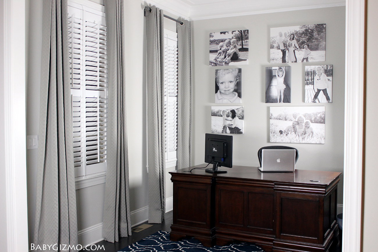 Grey office with large wood desk, grey drapes and a wall of black and white family portraits.
