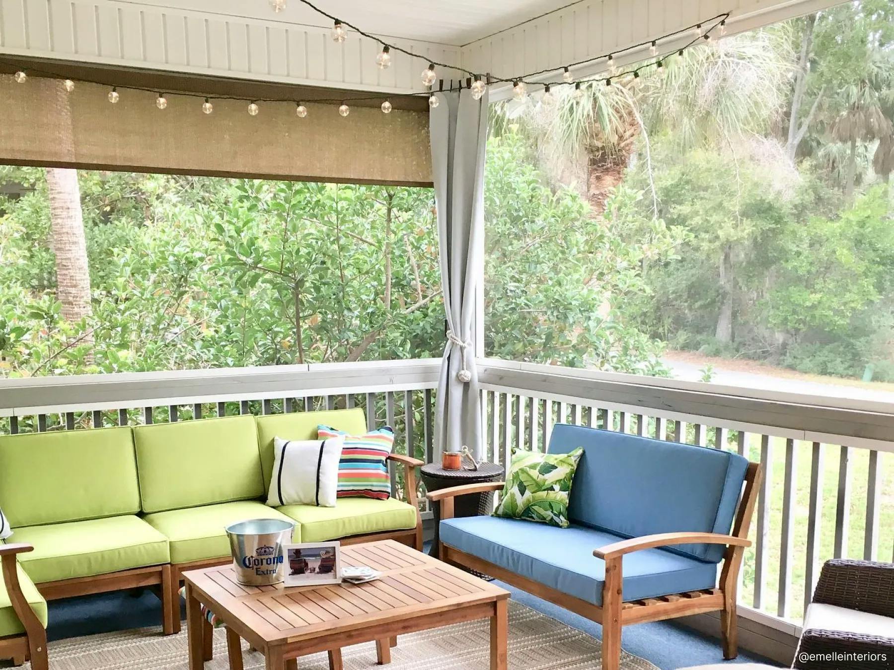Outdoor patio with outdoor furniture. The two outdoor couches have green and blue cushions. String lights hang from the roof. An outdoor shade is mounted between the pillars.