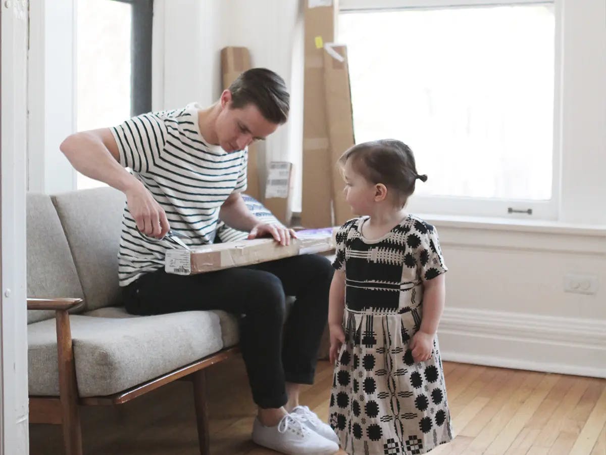 A man opens a package on a couch while a young girl watches.