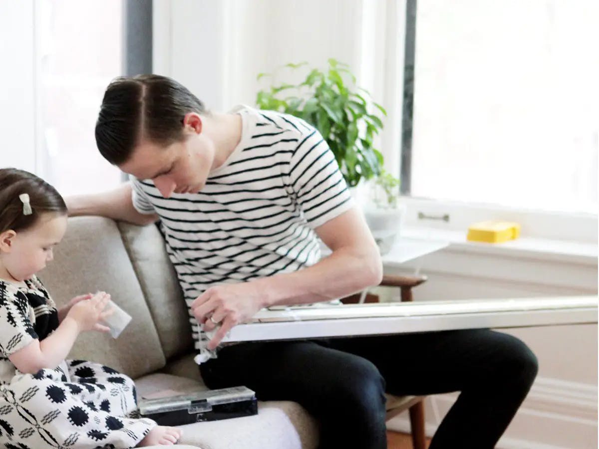 Man assembling blinds next to a young child on a couch.