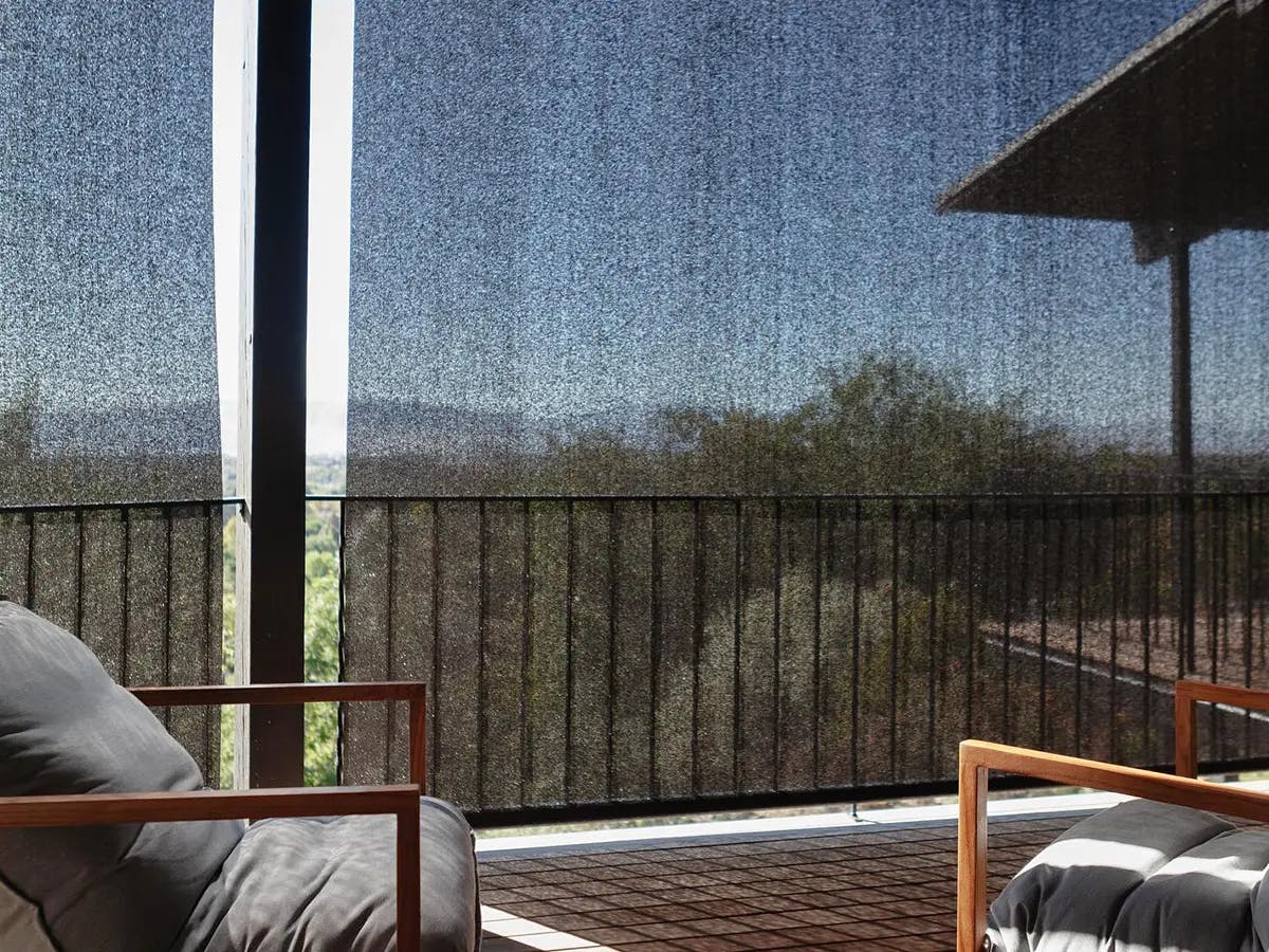 Balcony with gray and wooden furniture. Black, outdoor shades block the glare without blocking the view.