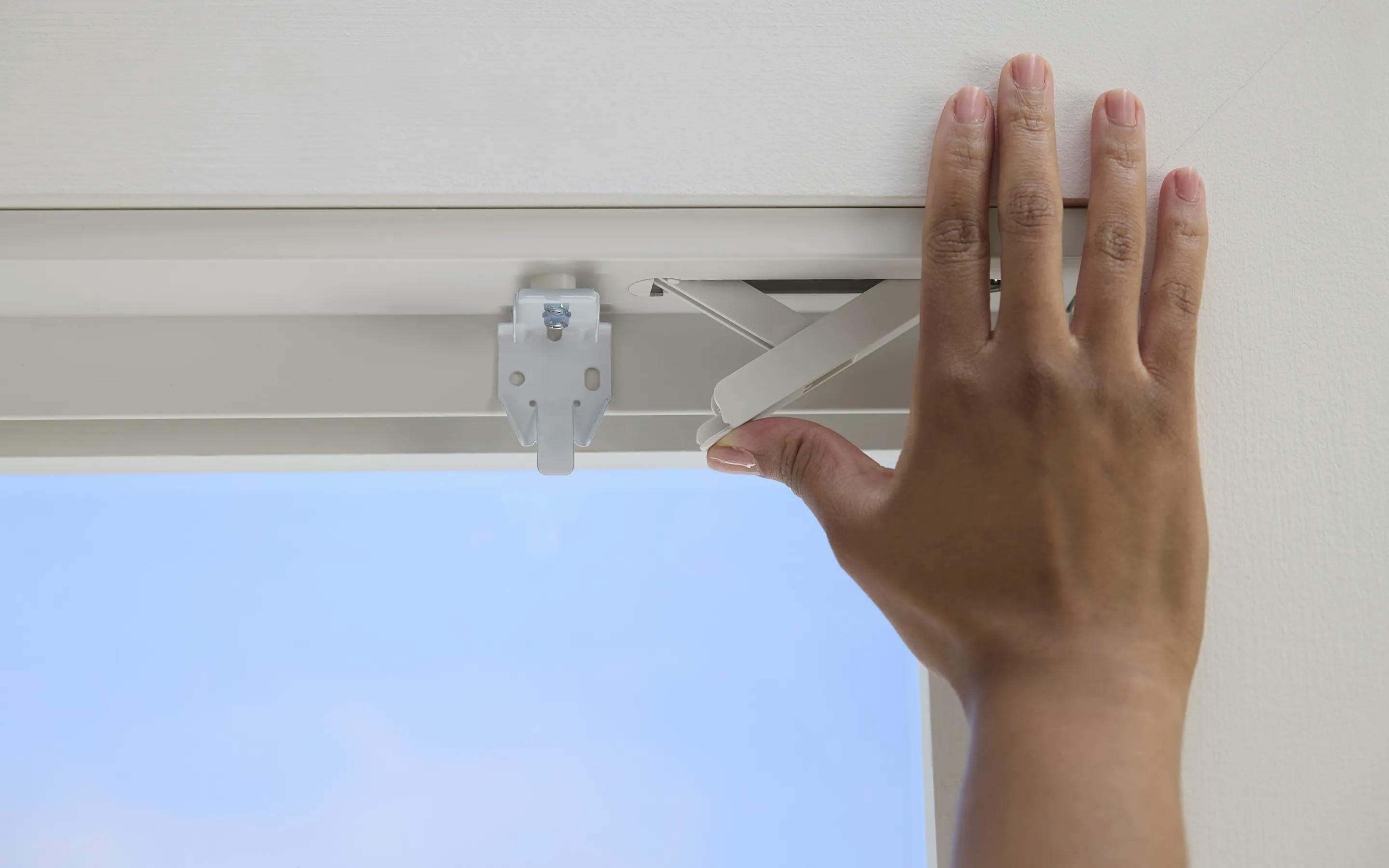 A hand using the close-tension no-drill mounting hardware on their new window treatments.