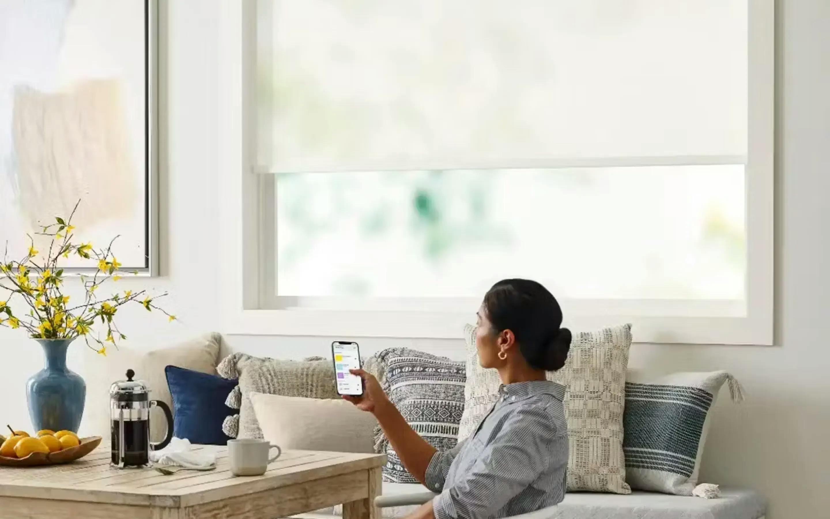 Woman using her phone to control the cellular shades on the window behind her.