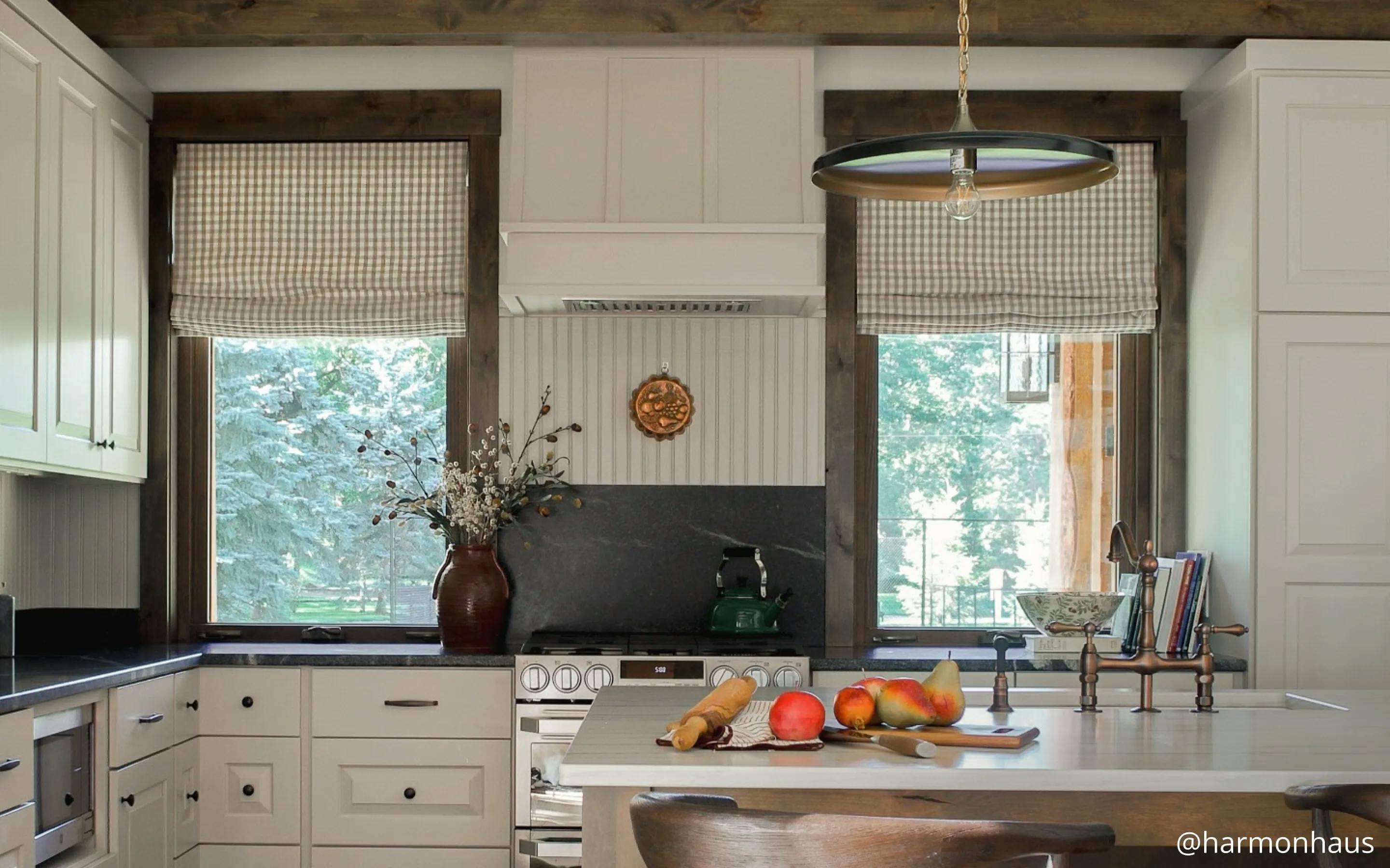 Kitchen with dark tones. The windows on either side of the stove feature patterned, neutral roman shades.
