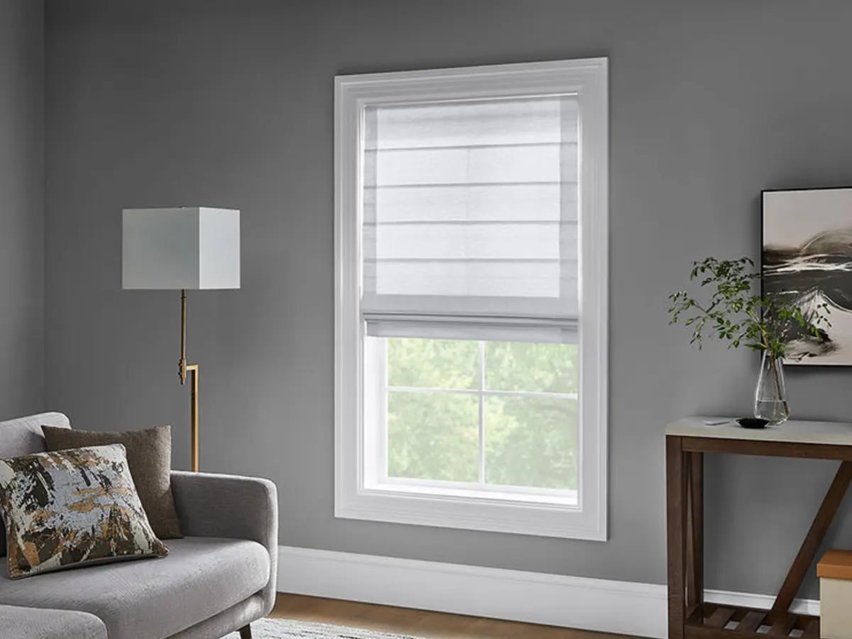 A room with a shades, a lamp and couch.