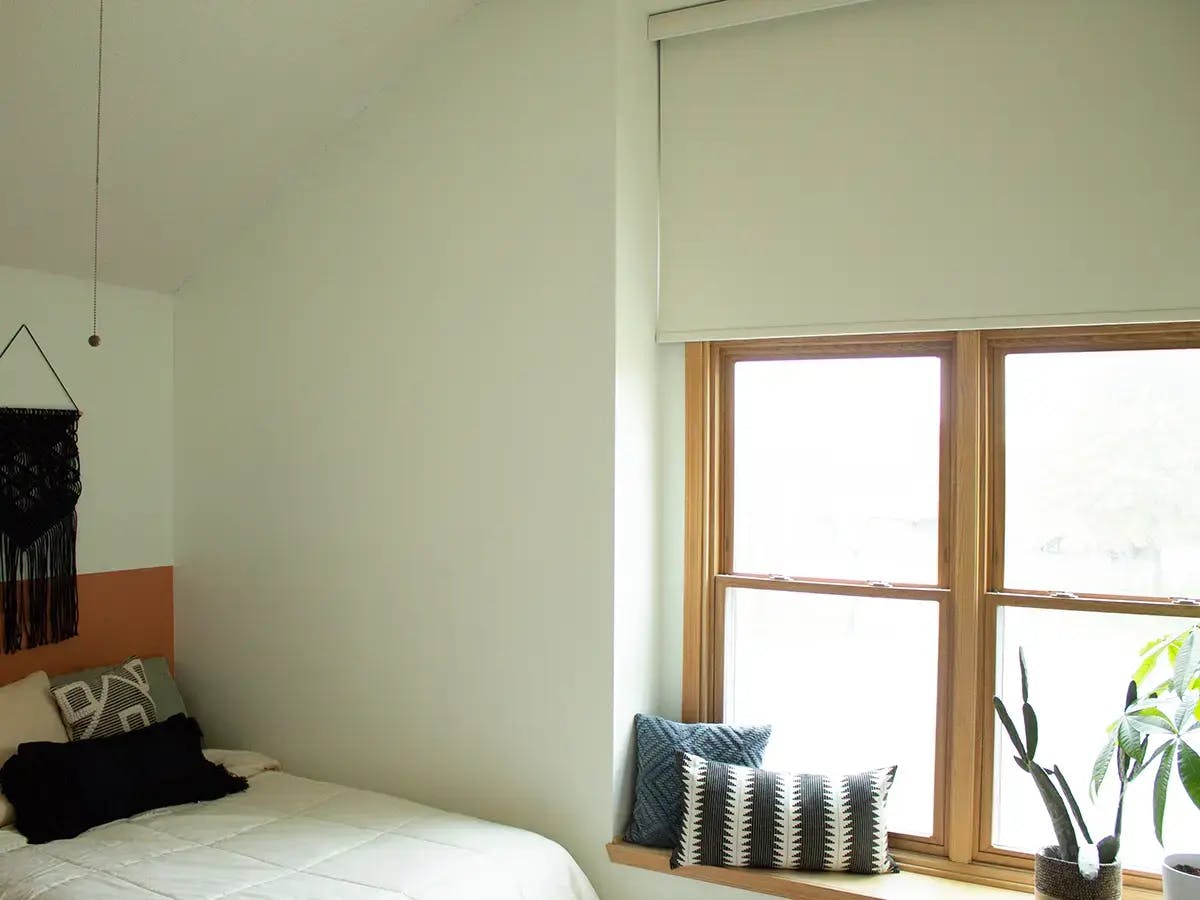 A bedroom with shades and a plant in the windowsill.