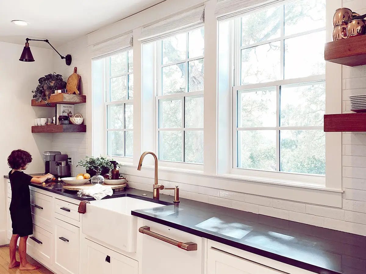 A modern kitchen with shades and a young child on the far left.