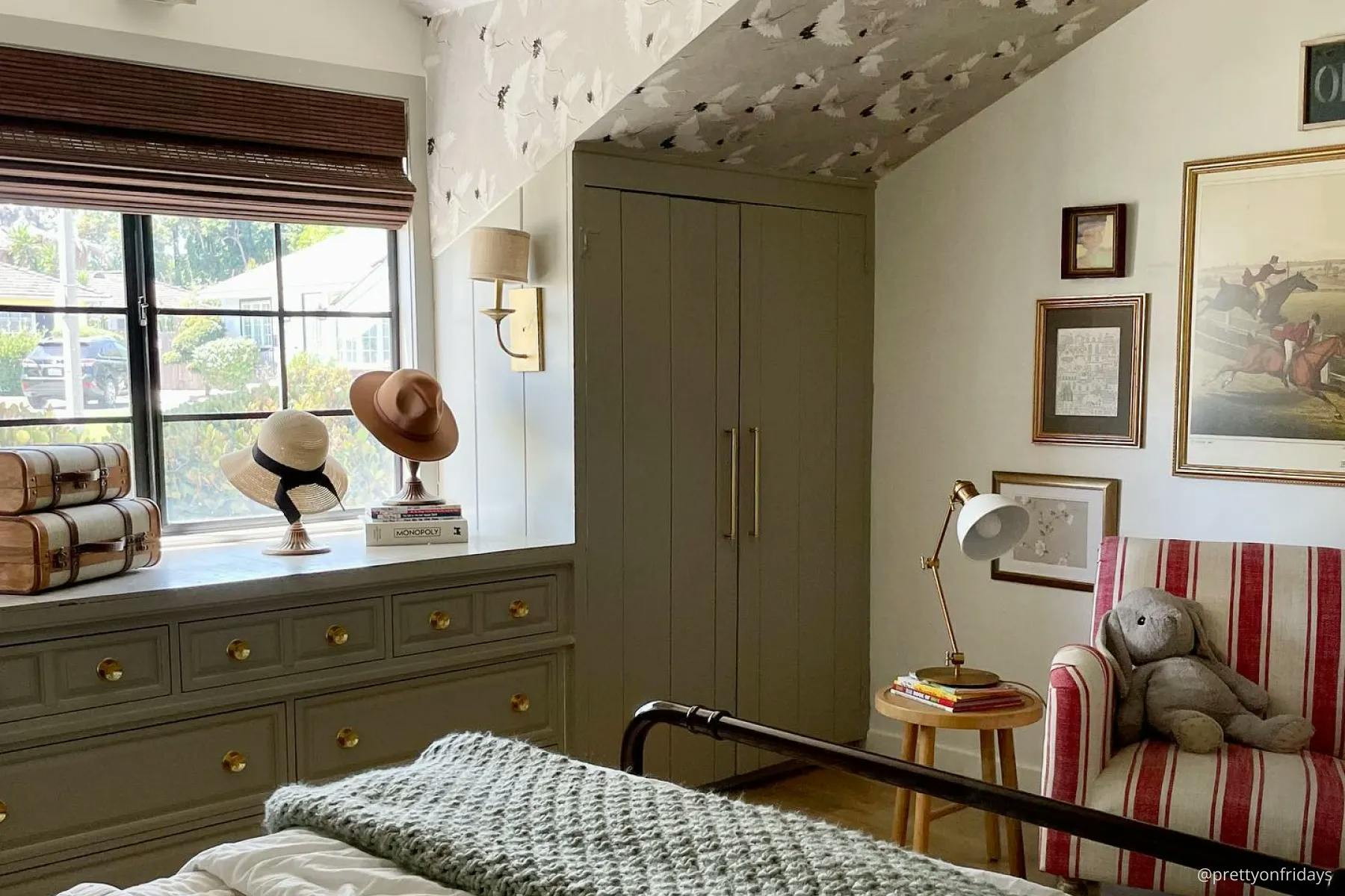 Bedroom with sage green wall paneling, neutral browns and creams and a cottagecore aesthetic. The window is covered with dark brown woven wood shades.