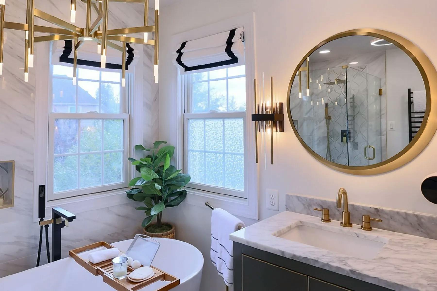 Bathroom with gold and marble accents, geometric shapes and an overall art-deco style. The windows are covered with black and white Roman shades.
