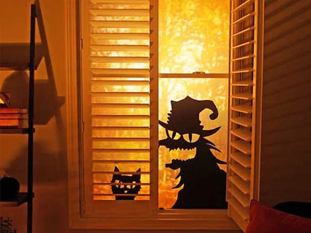 Window with Halloween silhouettes of a witch and a cat lit by an orange glow.