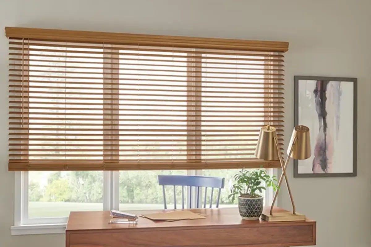Home office with faux wood blinds covering a wide window above a desk.