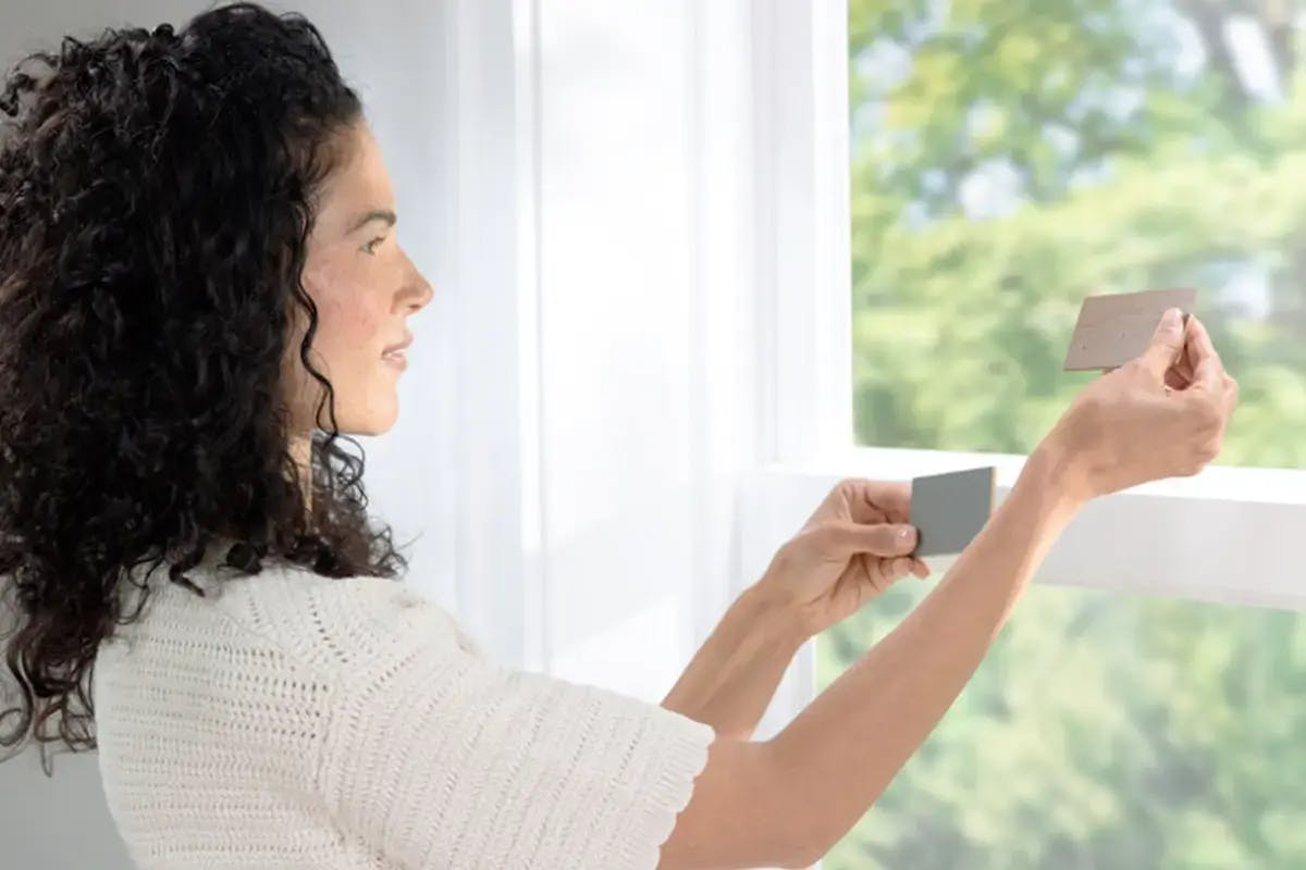 Woman holding paint swatches up to a window.