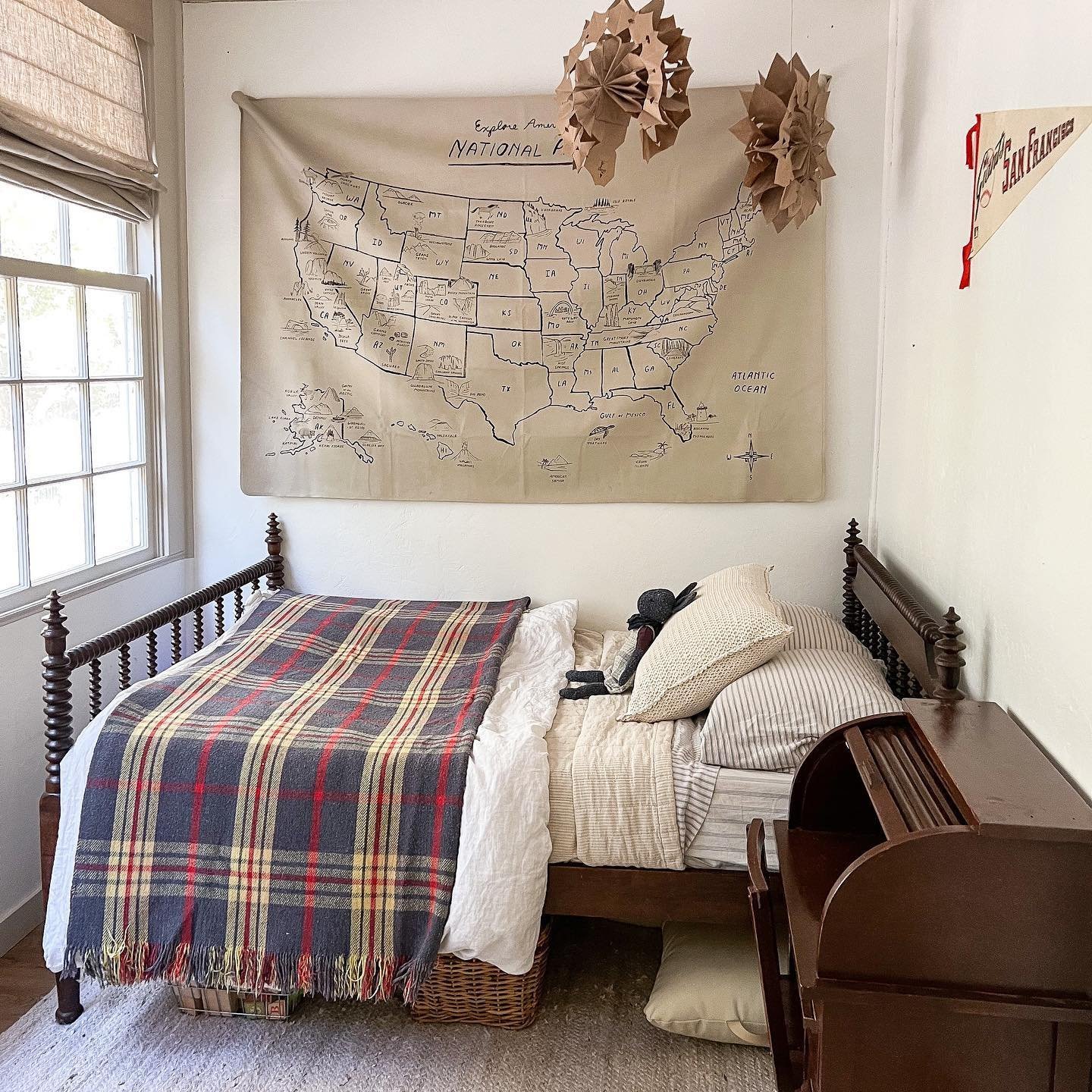 Fall house ideas. A child's bedroom with a dark plaid blanket draped over the bed. There is a large map on the wall. The bed is facing the window with Premium Roman shades from Blinds.com.