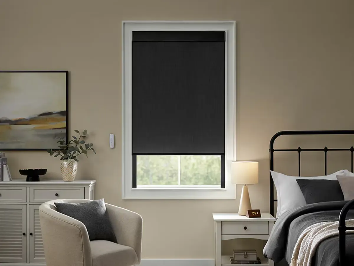 A modern bedroom featuring a black motorized blackout roller shade partially closed over a window.