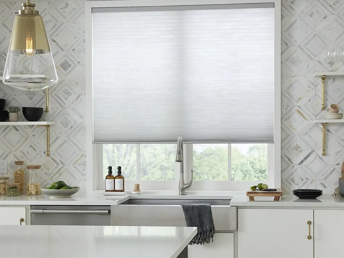 A bright kitchen featuring a white cellular honeycomb shade covering a large window.