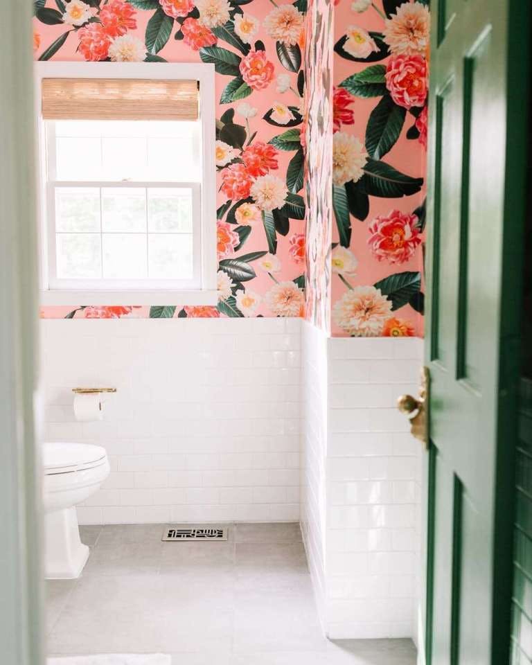 bathroom with large scale pink floral wallpaper, green door, white subway tile up wall and woven wood shades on window